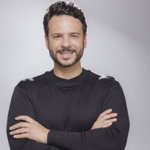 Foto de Israel Batista, do Todos pela Educação. Homem jovem de pele clara, com barba, bigode e cabelos castanho escuro. Atrás, fundo branco.